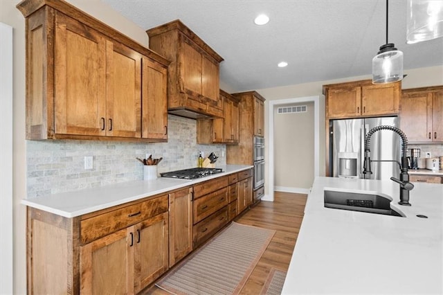 kitchen with sink, hanging light fixtures, decorative backsplash, appliances with stainless steel finishes, and light hardwood / wood-style floors