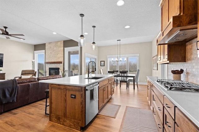 kitchen with backsplash, stainless steel appliances, a kitchen island with sink, pendant lighting, and light hardwood / wood-style floors