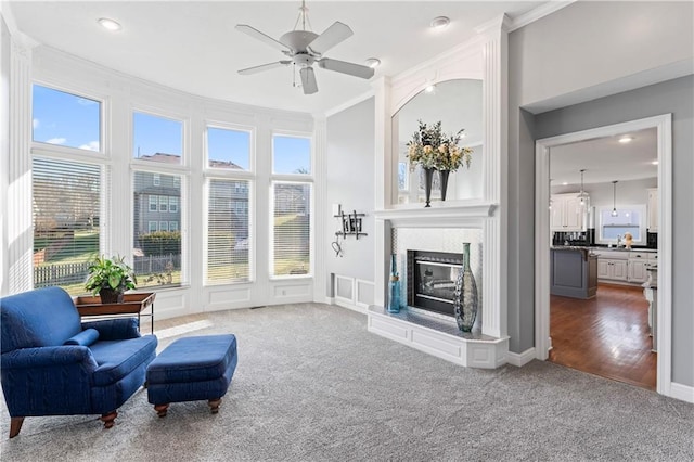 interior space featuring a large fireplace, carpet, a ceiling fan, and crown molding