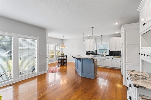 kitchen featuring pendant lighting, a center island, light stone countertops, and white cabinets