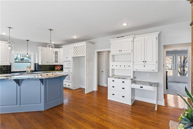 kitchen with white appliances, white cabinets, dark stone countertops, glass insert cabinets, and pendant lighting