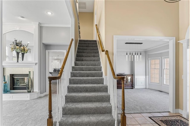 staircase featuring tile patterned floors, carpet, a glass covered fireplace, and crown molding