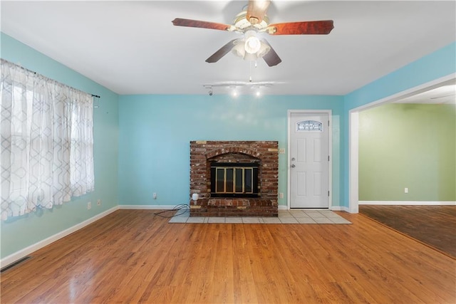 unfurnished living room with rail lighting, ceiling fan, a fireplace, and light hardwood / wood-style flooring