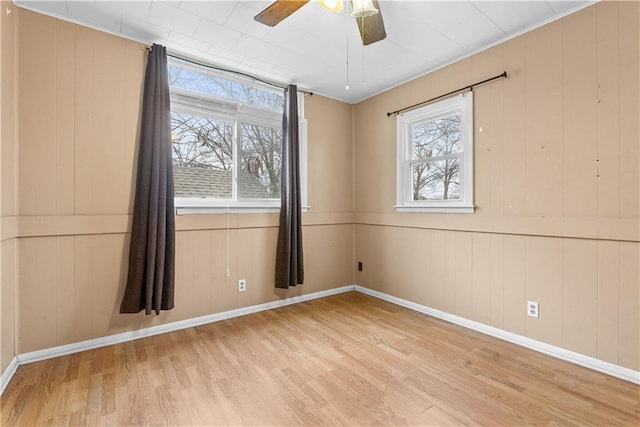 unfurnished room with ceiling fan, wood walls, and light wood-type flooring