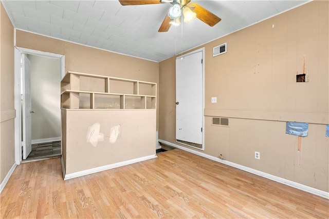 interior space featuring light wood-type flooring, ceiling fan, and wood walls