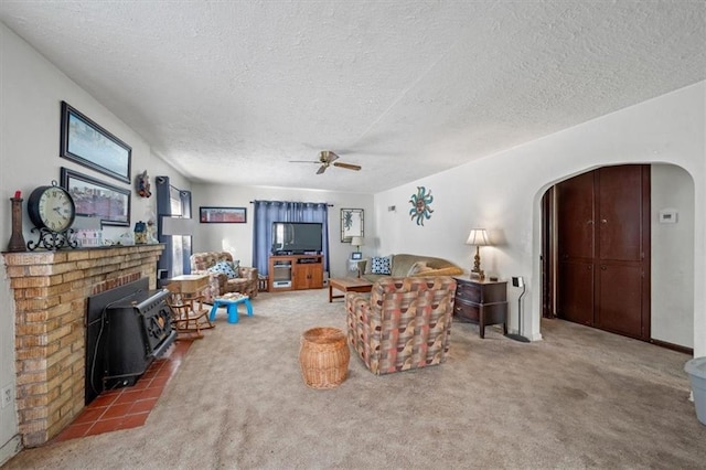 carpeted living room featuring a textured ceiling, a wood stove, and ceiling fan