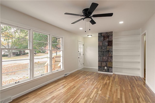 unfurnished room featuring built in shelves, light wood-type flooring, and ceiling fan