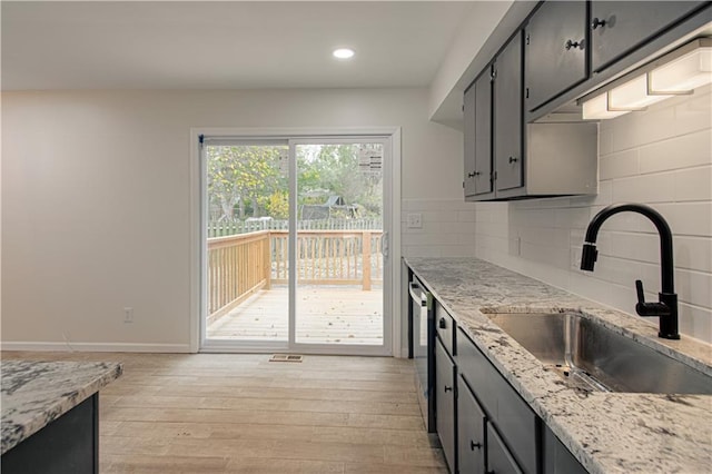 kitchen featuring light stone countertops, backsplash, stainless steel dishwasher, sink, and light hardwood / wood-style floors