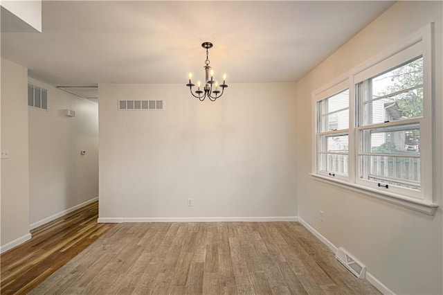 empty room featuring wood-type flooring and an inviting chandelier