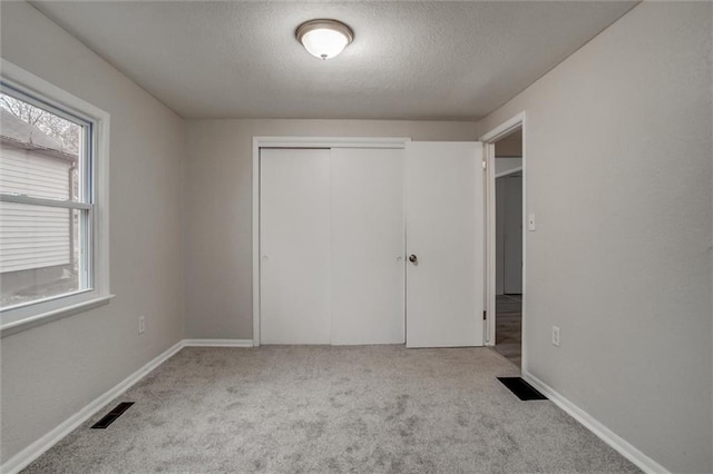 unfurnished bedroom with a closet, light colored carpet, and a textured ceiling