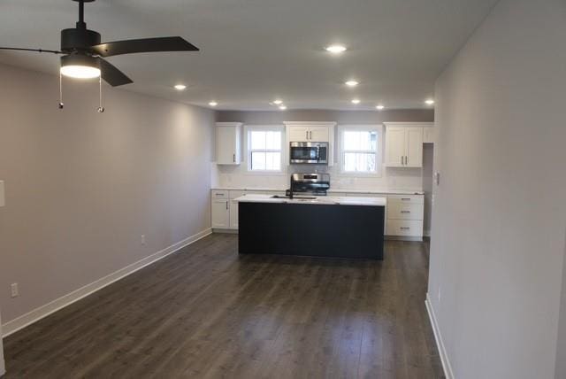 kitchen with decorative backsplash, stainless steel appliances, a kitchen island with sink, dark wood-type flooring, and white cabinets