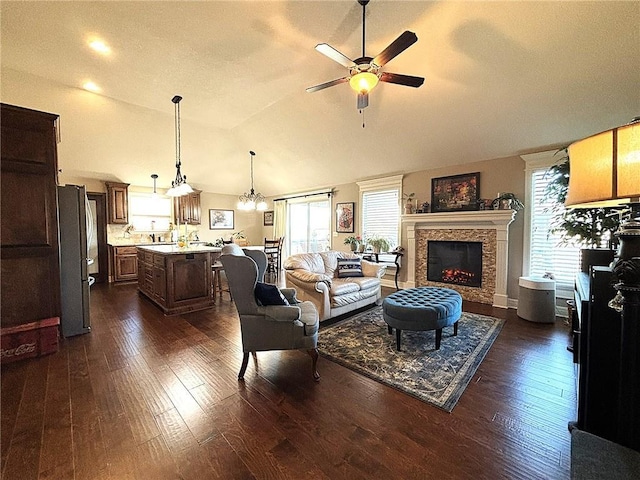 living room featuring ceiling fan with notable chandelier, vaulted ceiling, and dark wood-type flooring