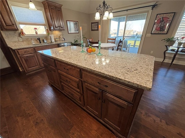 kitchen featuring hanging light fixtures, light stone countertops, a notable chandelier, a kitchen island, and dark hardwood / wood-style flooring