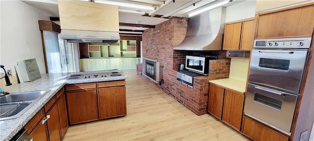 kitchen featuring light wood-type flooring, kitchen peninsula, brick wall, light stone counters, and appliances with stainless steel finishes