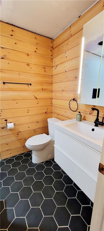 bathroom with toilet, wood walls, and vanity