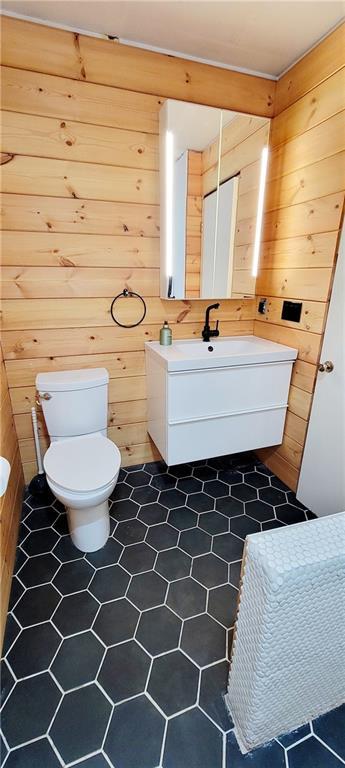 bathroom with toilet, wooden walls, tile patterned flooring, and vanity