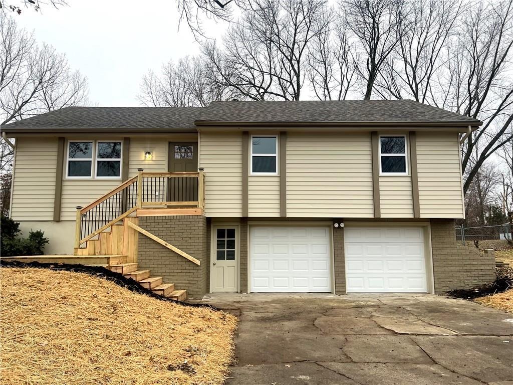 view of front of house with brick siding, a shingled roof, an attached garage, driveway, and stairs