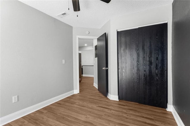 unfurnished bedroom with ceiling fan, a closet, wood-type flooring, and a textured ceiling