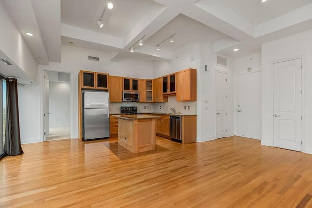 kitchen with a high ceiling, decorative backsplash, light hardwood / wood-style floors, appliances with stainless steel finishes, and a kitchen island