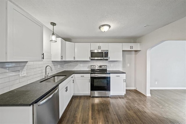 kitchen featuring sink, dark wood-type flooring, hanging light fixtures, white cabinets, and appliances with stainless steel finishes