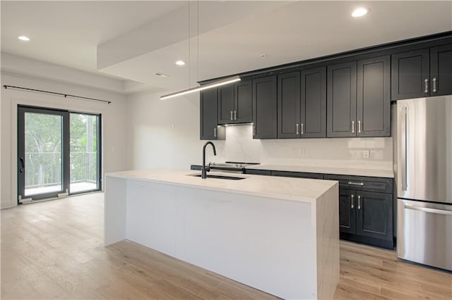 kitchen with pendant lighting, sink, an island with sink, tasteful backsplash, and stainless steel refrigerator