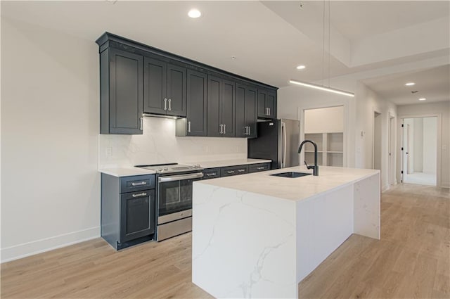 kitchen with a kitchen island with sink, sink, light hardwood / wood-style flooring, light stone countertops, and appliances with stainless steel finishes