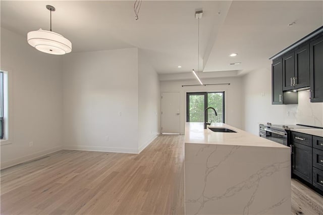 kitchen featuring pendant lighting, a kitchen island with sink, sink, light hardwood / wood-style floors, and light stone counters