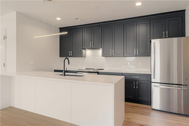 kitchen featuring sink, hanging light fixtures, light hardwood / wood-style flooring, tasteful backsplash, and stainless steel appliances