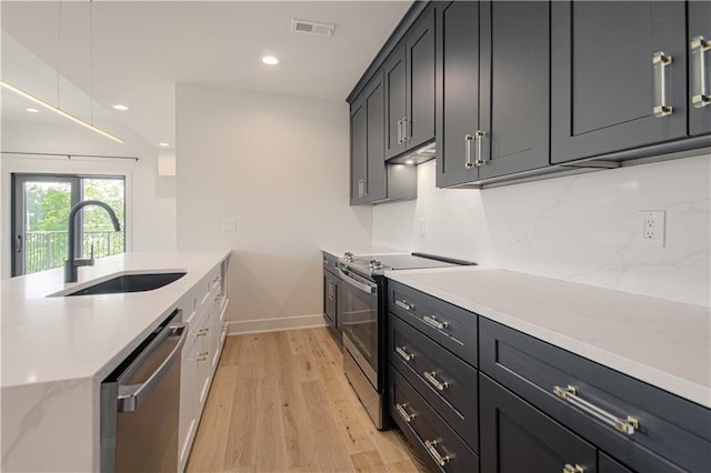 kitchen with light stone countertops, decorative backsplash, stainless steel appliances, sink, and light hardwood / wood-style flooring