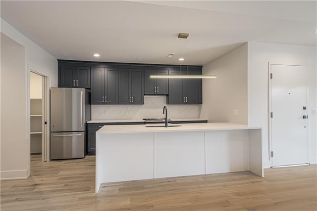 kitchen with sink, stainless steel fridge, decorative light fixtures, decorative backsplash, and light wood-type flooring