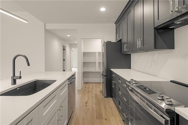 kitchen with backsplash, sink, light hardwood / wood-style flooring, light stone countertops, and stainless steel appliances