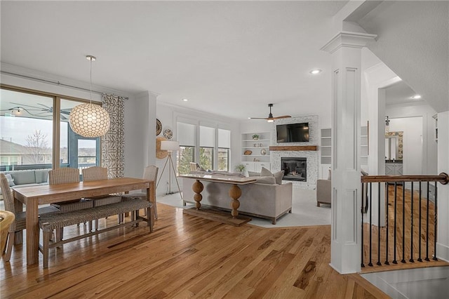 dining room with built in shelves, crown molding, decorative columns, light wood finished floors, and a stone fireplace