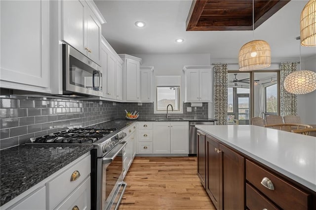 kitchen featuring tasteful backsplash, appliances with stainless steel finishes, light wood-type flooring, white cabinetry, and a sink