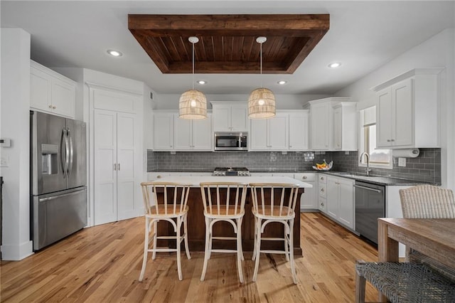 kitchen featuring white cabinets, a raised ceiling, decorative backsplash, appliances with stainless steel finishes, and a kitchen breakfast bar