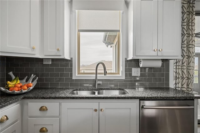 kitchen featuring tasteful backsplash, white cabinets, dark stone countertops, stainless steel dishwasher, and a sink