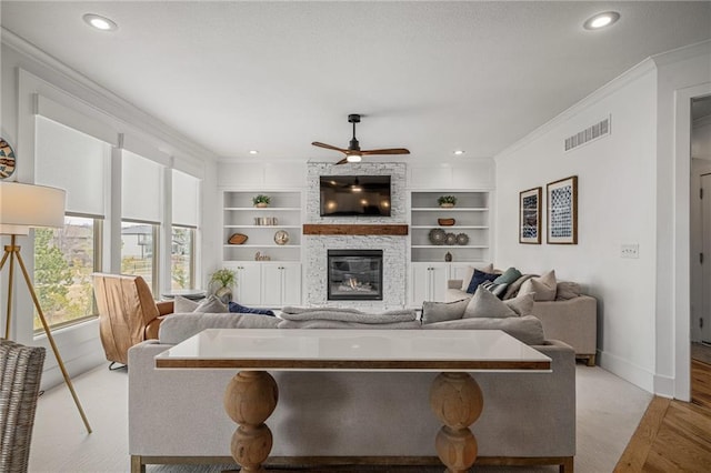 living room featuring built in shelves, a stone fireplace, visible vents, baseboards, and crown molding