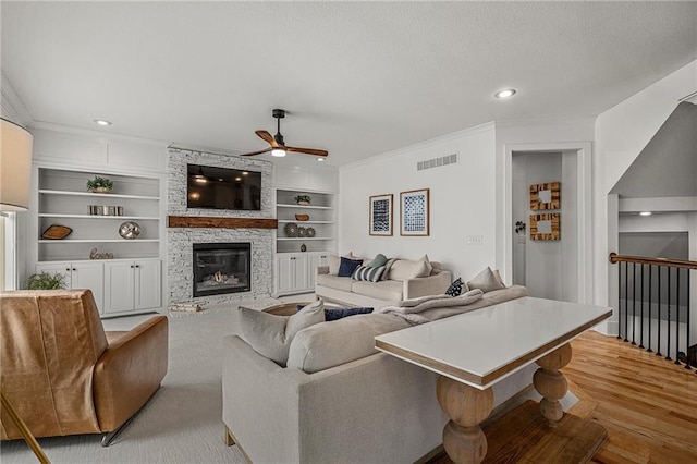 living area featuring a textured ceiling, built in shelves, a stone fireplace, visible vents, and crown molding