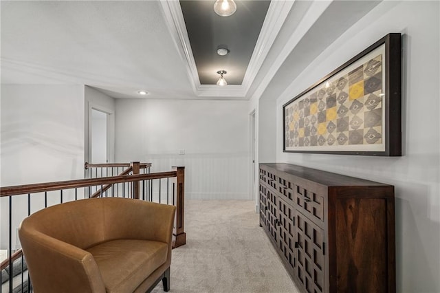 hall featuring light carpet, a raised ceiling, a wainscoted wall, crown molding, and an upstairs landing