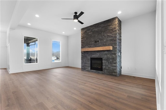 unfurnished living room featuring ceiling fan, a stone fireplace, baseboards, and wood finished floors