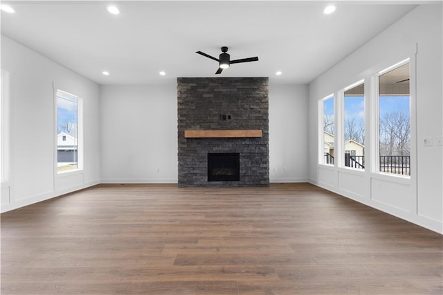 unfurnished living room featuring recessed lighting, a ceiling fan, a stone fireplace, wood finished floors, and baseboards