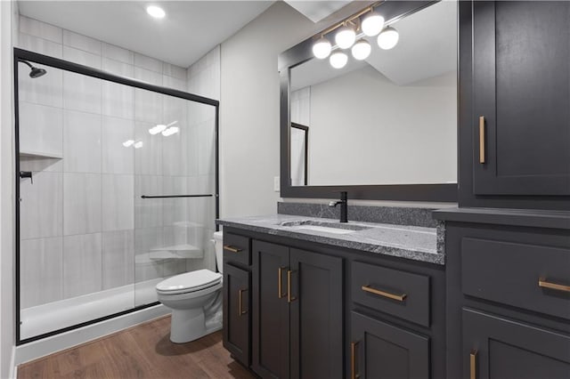 full bathroom featuring wood finished floors, a stall shower, vanity, and toilet