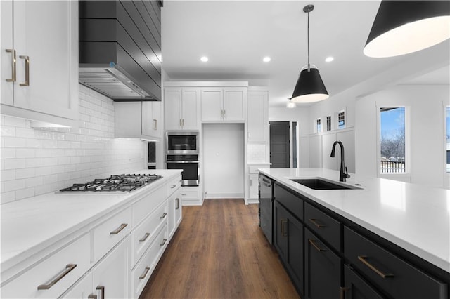 kitchen with dark cabinets, stainless steel appliances, a sink, hanging light fixtures, and wall chimney exhaust hood