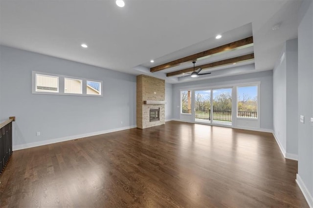 unfurnished living room featuring a fireplace, dark hardwood / wood-style flooring, ceiling fan, and beamed ceiling