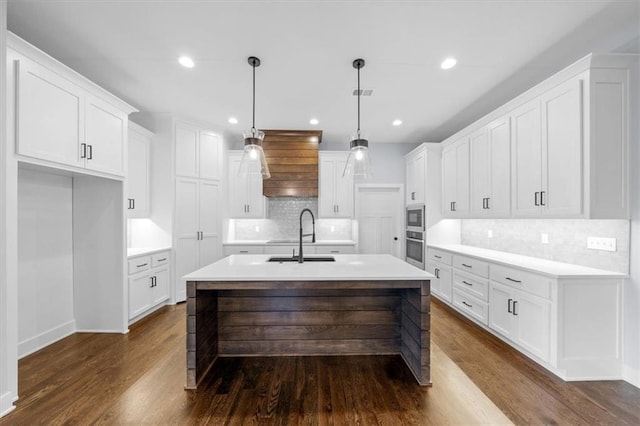 kitchen with an island with sink, appliances with stainless steel finishes, hanging light fixtures, light countertops, and white cabinetry