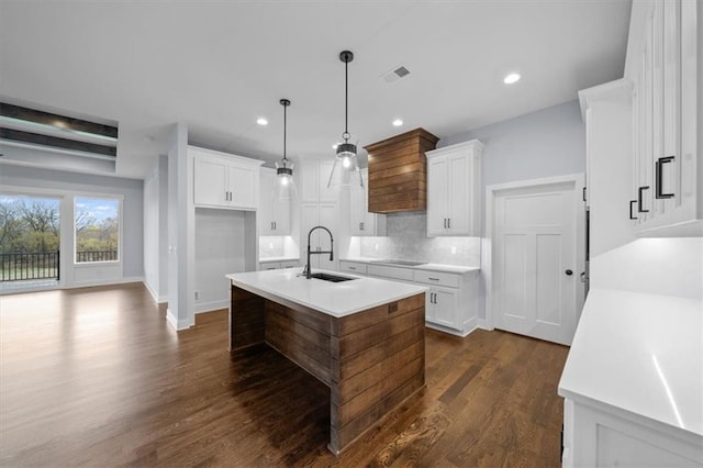 kitchen with a sink, white cabinets, light countertops, hanging light fixtures, and an island with sink