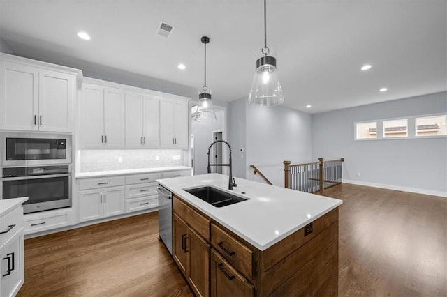 kitchen with a center island with sink, white cabinets, stainless steel appliances, light countertops, and a sink