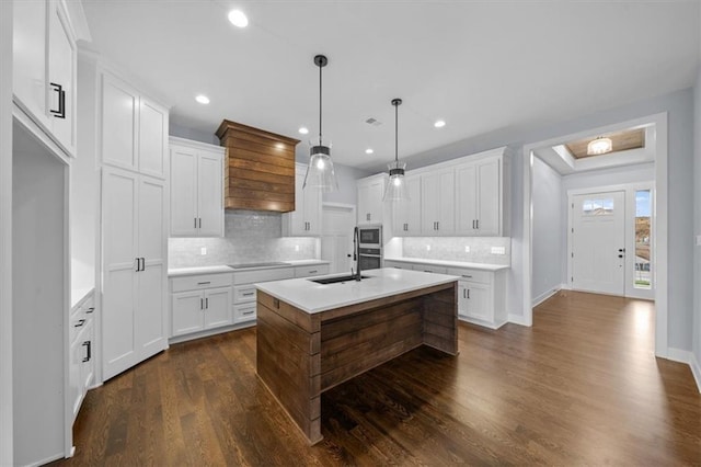 kitchen with dark wood-style flooring, white cabinets, light countertops, an island with sink, and pendant lighting