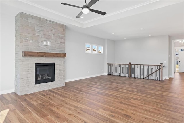 unfurnished living room with baseboards, a raised ceiling, wood finished floors, and a stone fireplace