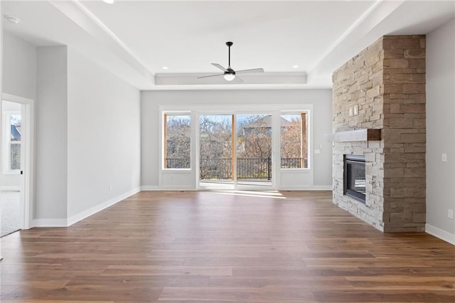 unfurnished living room with a fireplace, a ceiling fan, a raised ceiling, and dark wood-style flooring