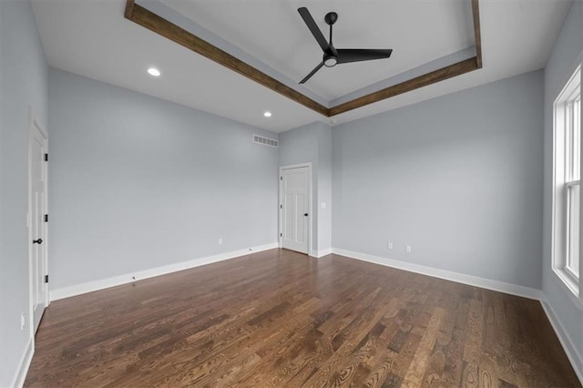 empty room featuring dark wood-style floors, baseboards, visible vents, and a raised ceiling